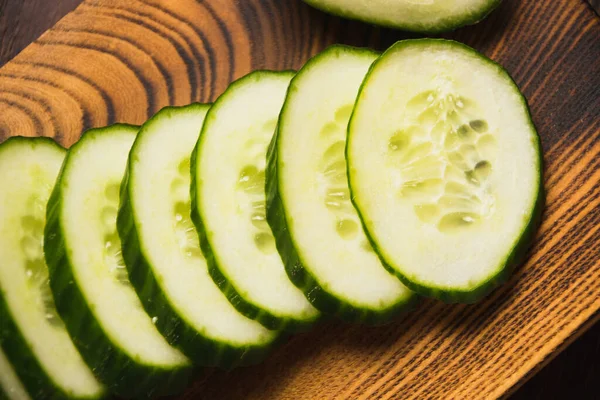Flatlay, sliced cucumber on a dark wooden board in rustic style, cucumber slices close-up.