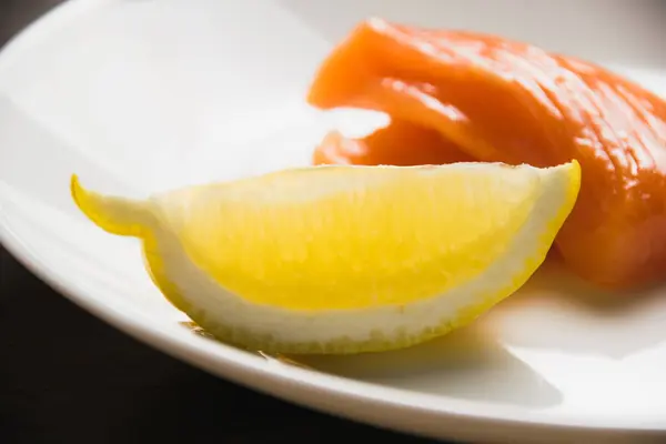 ジューシーなレモンのくさびと 背景には白いプレート上の赤い魚の破片 — ストック写真