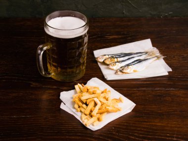 Bira bardağında nefis hafif bira, krakerler ve siyah arka planda kurutulmuş balık..