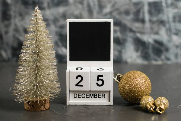 Wooden calendar with December 25 date and beautiful Christmas decoration on dark textured background with copy space.