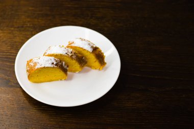 Lezzetli balkabaklı kek. Koyu ahşap bir masada beyaz bir tabakta parçalara ayrılmış..