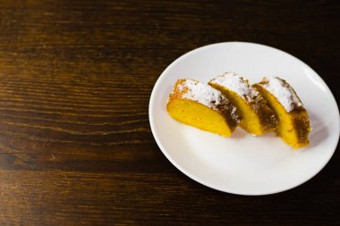 Lezzetli balkabaklı kek. Koyu ahşap bir masada beyaz bir tabakta parçalara ayrılmış..