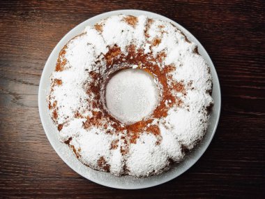 Koyu ahşap bir masada beyaz bir tabağa pudra şekeri serpiştirilmiş lezzetli balkabaklı kek..