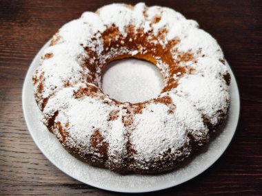 Koyu ahşap bir masada beyaz bir tabağa pudra şekeri serpiştirilmiş lezzetli balkabaklı kek..