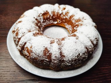 Koyu ahşap bir masada beyaz bir tabağa pudra şekeri serpiştirilmiş lezzetli balkabaklı kek..