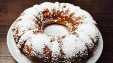 Koyu ahşap bir masada beyaz bir tabağa pudra şekeri serpiştirilmiş lezzetli balkabaklı kek..