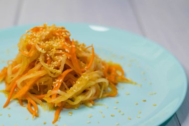 Delicious Korean cuisine. Salad with carrots and daikon Korean style on a beautiful turquoise plate clipart