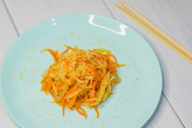 Delicious Korean cuisine. Salad with carrots and daikon Korean style on a beautiful turquoise plate clipart