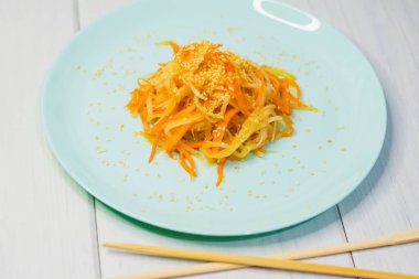 Delicious Korean cuisine. Salad with carrots and daikon Korean style on a beautiful turquoise plate clipart