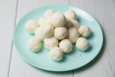 Hindistan cevizi gevrekleri ve bademlerle ev yapımı lezzetli şekerlerle dolu mavi tabak açık ahşap bir masada duruyor, arka planda kopya alanı var..