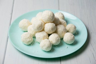 Hindistan cevizi gevrekleri ve bademlerle ev yapımı lezzetli şekerlerle dolu mavi tabak açık ahşap bir masada duruyor, arka planda kopya alanı var..