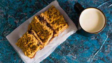 Elma reçelli nefis ev yapımı turta. Tahtaya reçel konmuş rendelenmiş turtanın iştah açıcı dilimleri ve masada bir fincan süt.