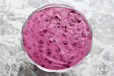 Açık arkaplanda şeffaf bir kasede pembe tatlı. Frenk üzümlü yaz tatlısı.