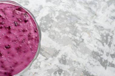 Açık arkaplanda şeffaf bir kasede pembe tatlı. Frenk üzümlü yaz tatlısı.