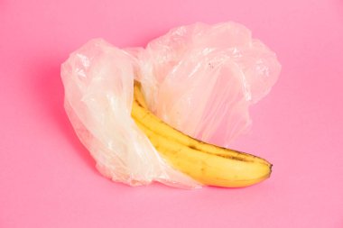 Pembe arka planda plastik bir torba içinde çürük derili muzlar..