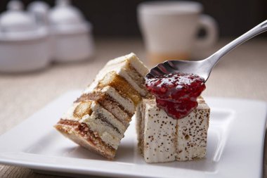 Beyaz bir tabakta servis edilen tiramisu kekinin üzerine çilekli jöle kaşık çekerken çekilmiş yakın çekim fotoğrafı..