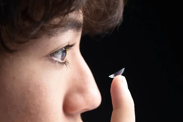 Extreme close up photo of a teenage boy holding up a contact lens in the act of putting it on.