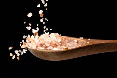 Yakın plan bir fotoğraf ahşap kaşığa dökülen pembe Himalaya deniz tuzu siyah arka plana karşı..