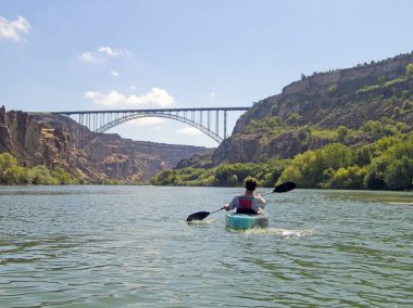 Genç bir çocuk, Idaho, Twin Falls 'daki Snake River' da güzel bir günde Perrine Köprüsü 'ne doğru kanoyla kürek çekiyor..