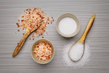 Düz bir fotoğraf Himalaya pembe tuzu ve kaba beyaz deniz tuzu kaseler ve tahta kaşıklar üzerinde yatıyordu..