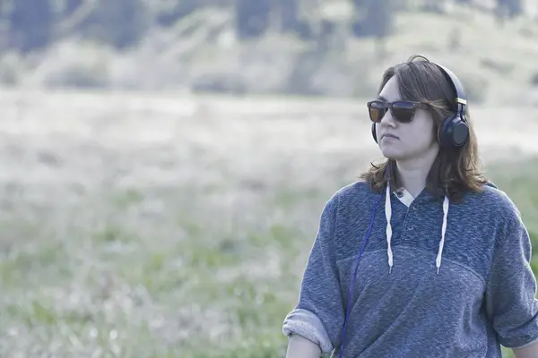 stock image A young woman wearing sunglasses on a bright day listens to music on her headphones while on a nature walk in Washington.