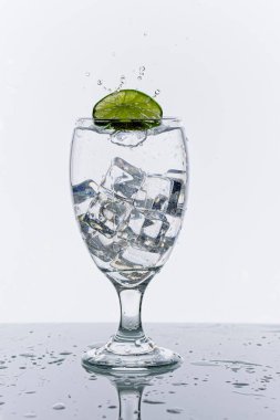 Stüdyo konsepti olan bir fotoğraf. Su bardağına bir dilim limon atıp su sıçratırken çekilmiş..