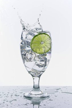 Stüdyo konsepti olan bir fotoğraf. Su bardağına bir dilim limon atıp su sıçratırken çekilmiş..