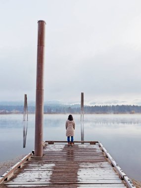 Paltolu bir kadın rıhtımın sonunda duruyor. Doğu Washington 'daki Pend Oreille Nehri' ne bakıyor..