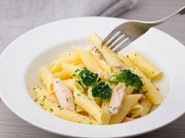 Parmesan peyniri, brokoli ve tavuk parçalarıyla kaplı lezzetli makarna dolu bir çatal alıyorum..