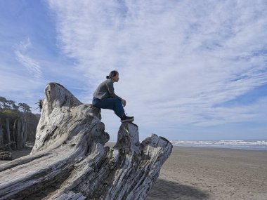 Orta yaşlı bir kadın, Washington eyaletinin Kalaloch bölgesi yakınlarındaki sahildeki büyük bir ağaç dalının tepesinde oturuyor..