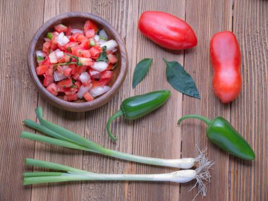 A flatlay photo of a bowl of salsa with whole tomatoes, peppers, and green onions.