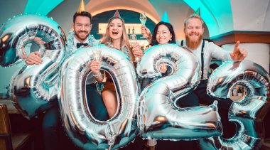 2023 'ün gelişini kutlayan bir grup parti insanı, kameraya bakan erkekler ve kadınlar