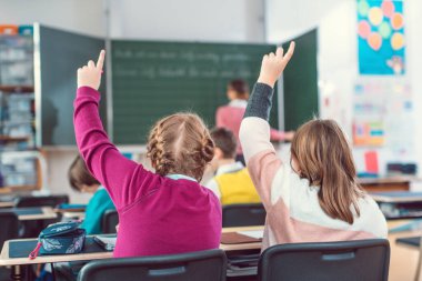 İki kız öğrenci bir soruyu cevaplamak için el kaldırıyor çünkü cevabı biliyorlar.