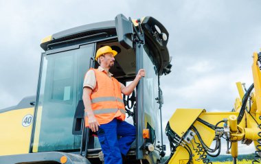 Şantiyede yapılacak işi planlayan ekskavatör üzerinde inşaat işçisi