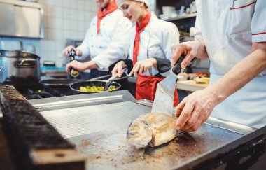 Mutfakta bir grup aşçı tavada harika yemekler hazırlıyor.