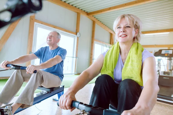 Senior couple in the gym on a rowing machine exercising for better fitness