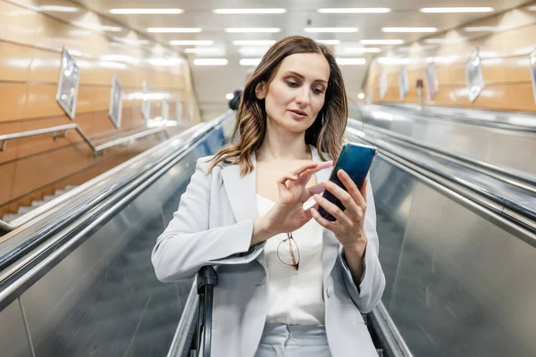 穿西服的女人拿着手机从自动扶梯下到地铁站 — 图库照片