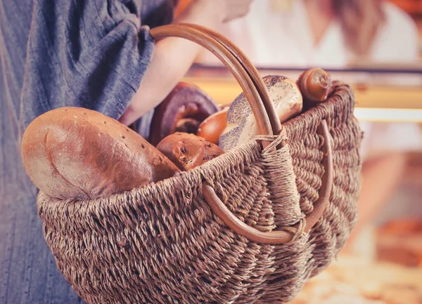 woman customer in a bakery shop with basket of fresh bread and rolls she just bought