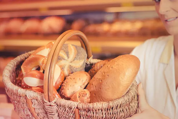 面包店里的女售货员 提着一篮子面包和面包卷 图库图片