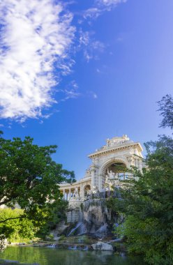 Longchamp Sarayı görkemli şelalesi ve canlı bir gökyüzü altında yemyeşil yapraklarla çerçevelenmiş ayrıntılı taş işçiliği. Marsilya 'daki bu mimari mucize doğayla uyum içinde, tarih ve güzellik vahası yaratıyor..