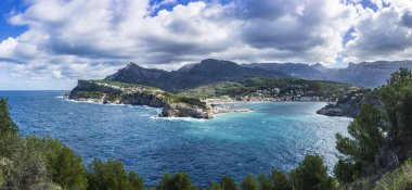 Port de Soller 'in dinamik kıyı şeridi, kayalık yapılar ve Serra de Tramuntana' nın geniş panoramik çekimi.