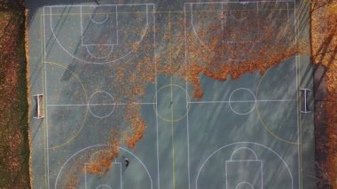Worker with leaf blower working on autumn basketball court, aerial view