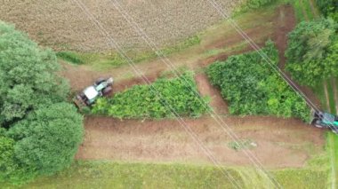 İki traktör, yüksek voltajlı bir elektrik hattının altındaki çalıları temizliyor.