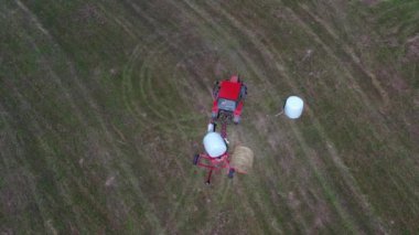 tarım traktörü bir saman balyasını plastikle kaplıyor, hava manzaralı.