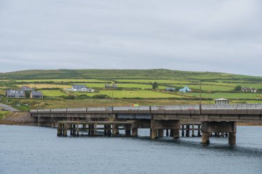 Portmagee, İrlanda - 7 Ağustos 2024. Yatay beton bir köprü, bulutlu bir sabah sisinin içinde yükselen bir tepe ile, arazi boyunca uzanır.