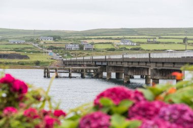 Portmagee, İrlanda - 7 Ağustos 2024. Yatay beton bir köprü, bulutlu bir sabah sisinin içinde yükselen bir tepe ile, arazi boyunca uzanır.