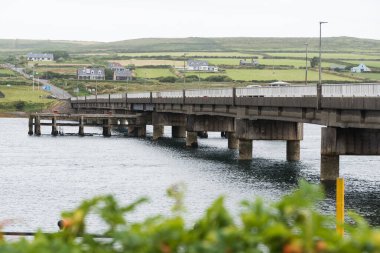 Portmagee, İrlanda - 7 Ağustos 2024. Yatay beton bir köprü, bulutlu bir sabah sisinin içinde yükselen bir tepe ile, arazi boyunca uzanır.