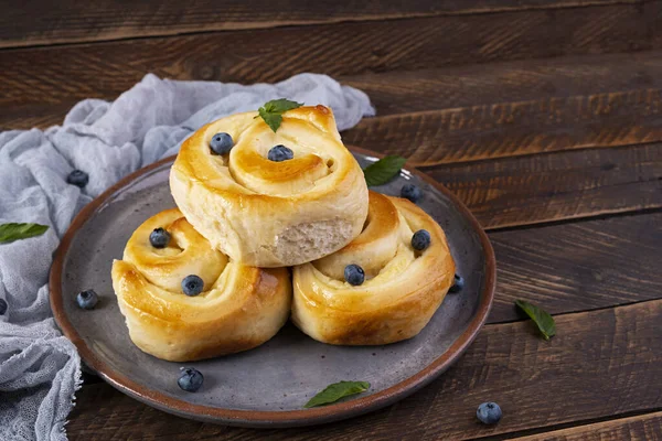Sweet buns with custard on wooden background. Custard buns with blueberries