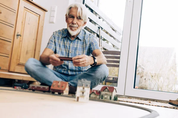 部屋でモデル蒸気機関車で遊んでいる高齢者の屋内肖像画 — ストック写真