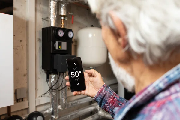 スマートホームコンセプト 彼の携帯電話上のアプリを使用して暖房システムを制御する男 — ストック写真